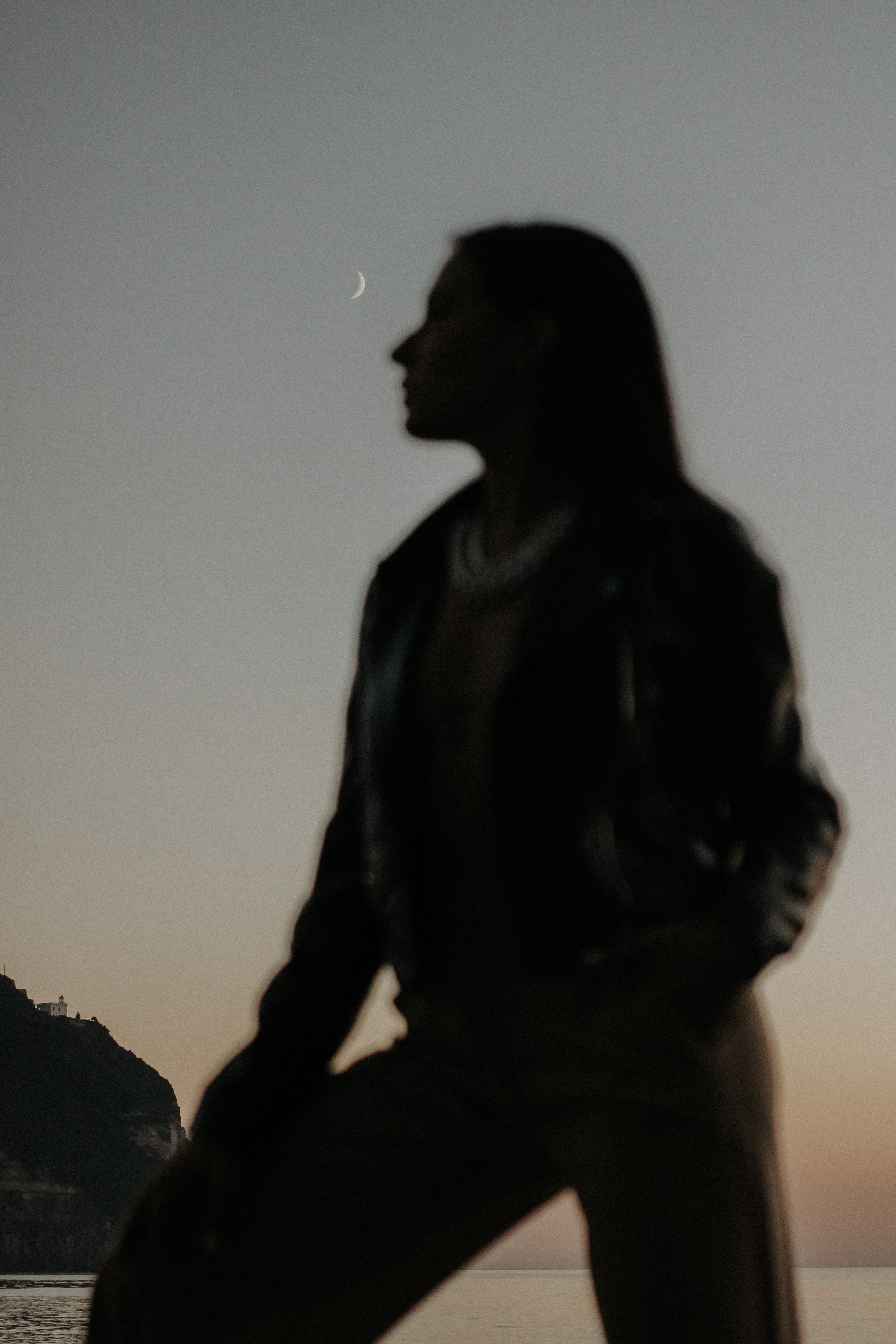 Silhouette of a woman against a crescent moon in a serene twilight sky.