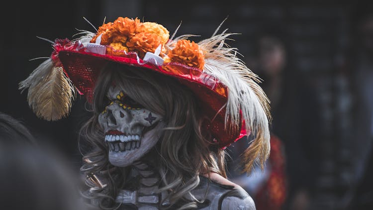 A Person With Skull Face Mask Wearing A Hat With Feathers And Flowers