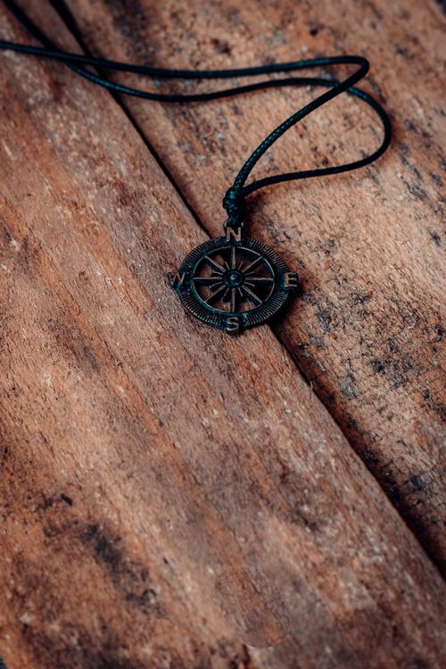 Free Close-up of a compass pendant on a wooden surface, symbolizing direction and exploration. Stock Photo