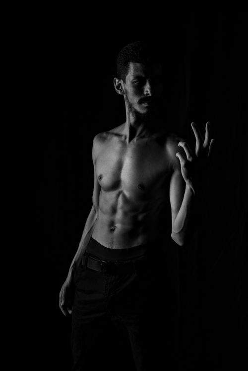 Free Black and white portrait of a shirtless man in a contemplative pose with a dark background. Stock Photo