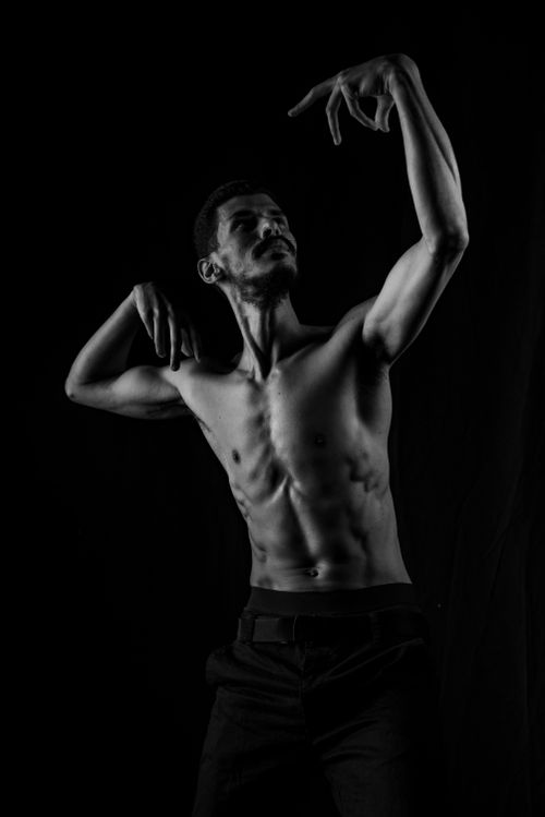 Free Artistic black-and-white portrait of a shirtless man striking a pose against a dark background. Stock Photo