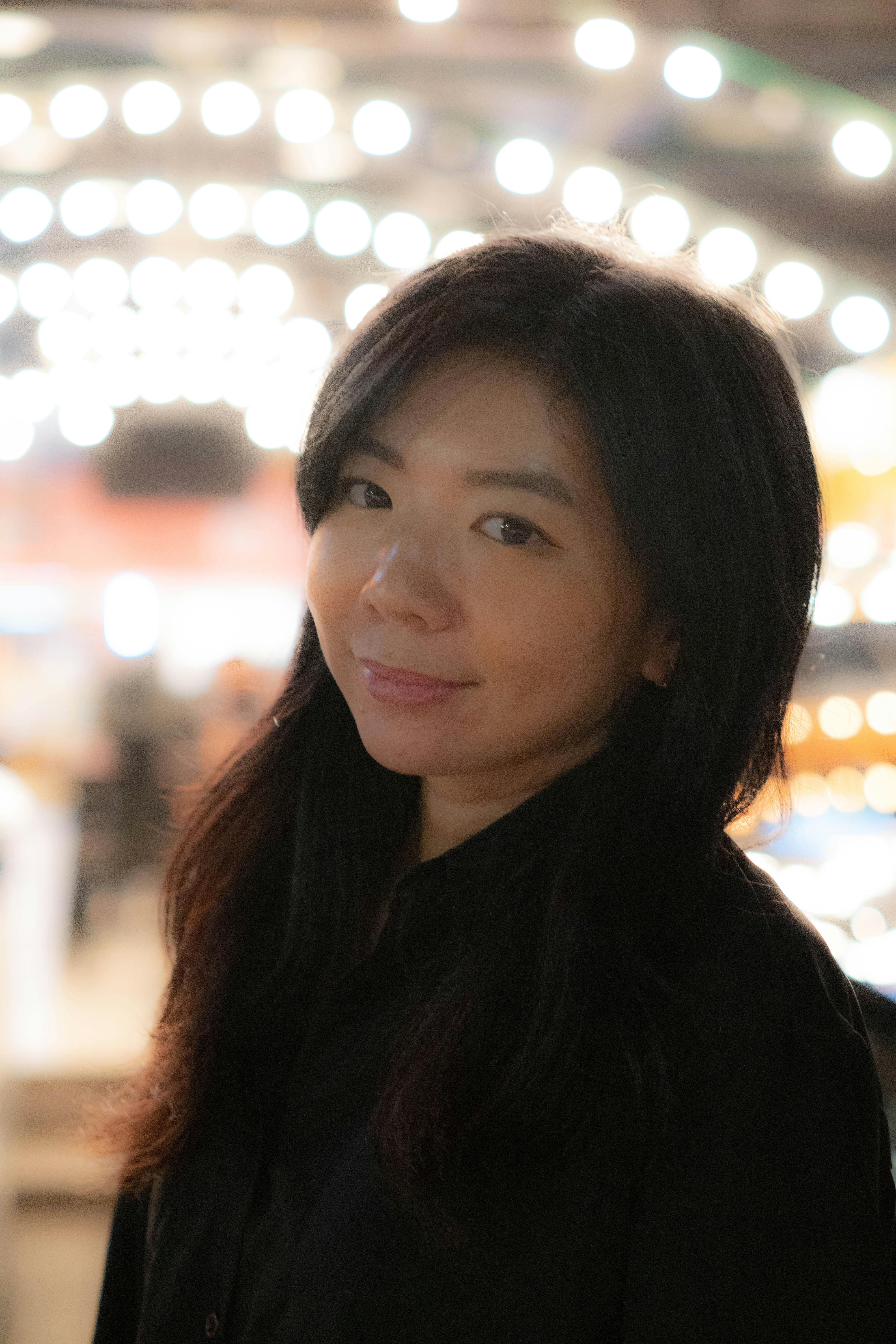 A woman smiles gently against a backdrop of glowing lights in Jakarta. Captured in a vibrant night setting.