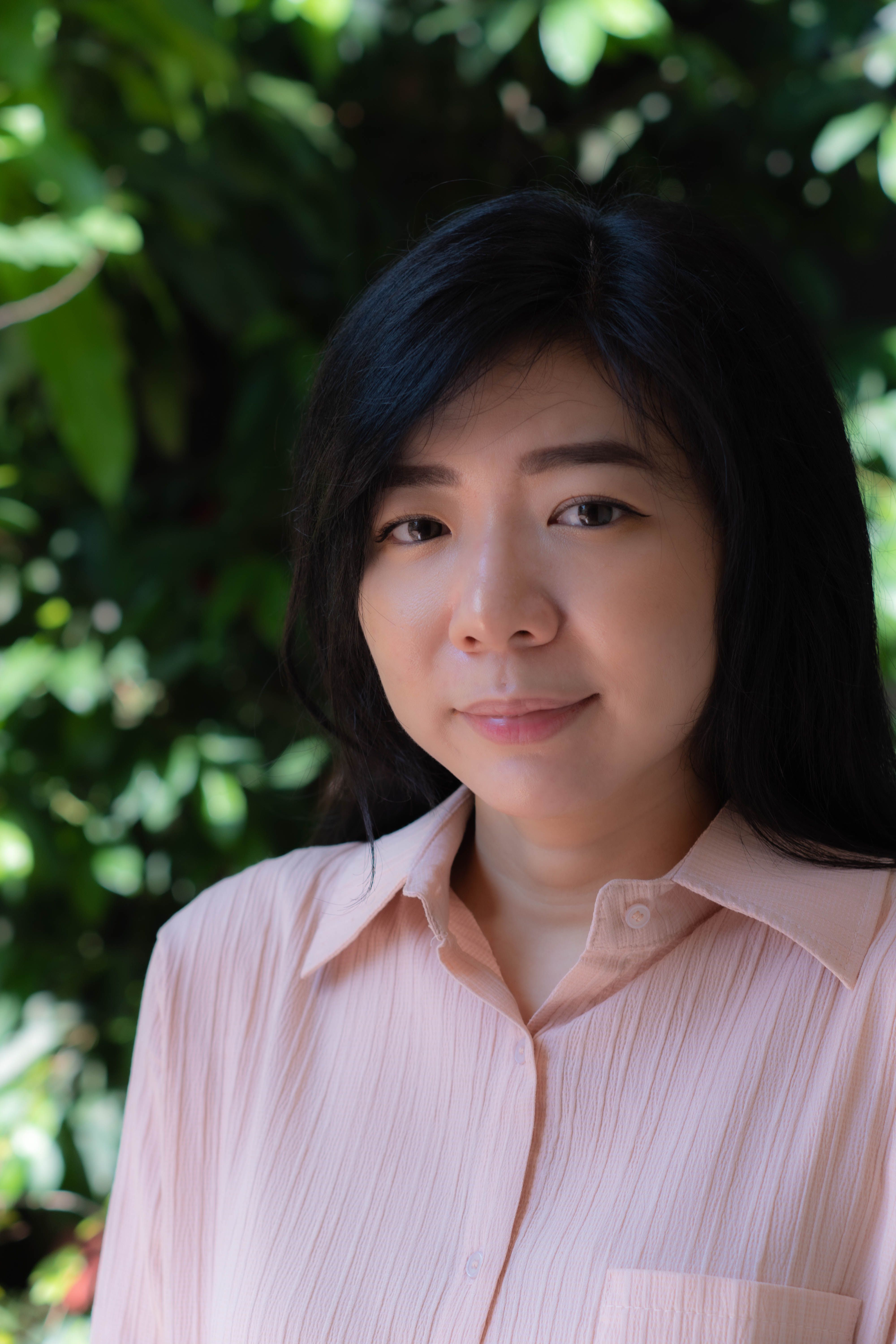 Portrait of an Asian woman smiling in a pink blouse outdoors in Jakarta.