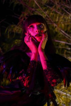 A woman in gothic fashion poses dramatically under vibrant pink lighting.