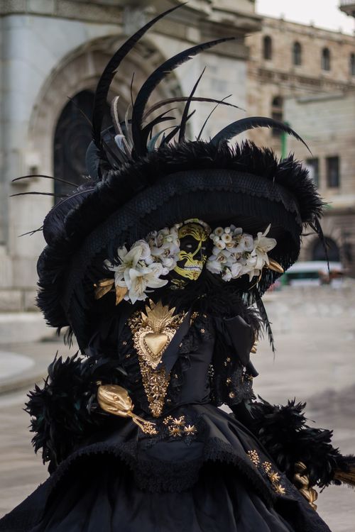 Free Ornate masquerade costume adorned with feathers and flowers, set in a historic urban backdrop. Stock Photo