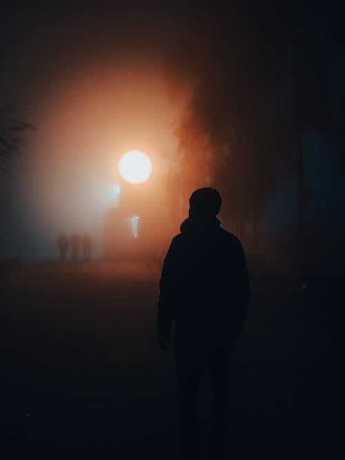 Silhouette of Man Standing on Road at Night Time