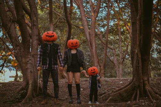 A family wearing pumpkin heads in a forest, embodying Halloween spirit.