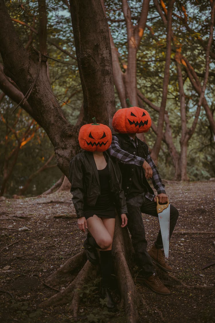 Two People Wearing Pumpkin Masks In A Forest 