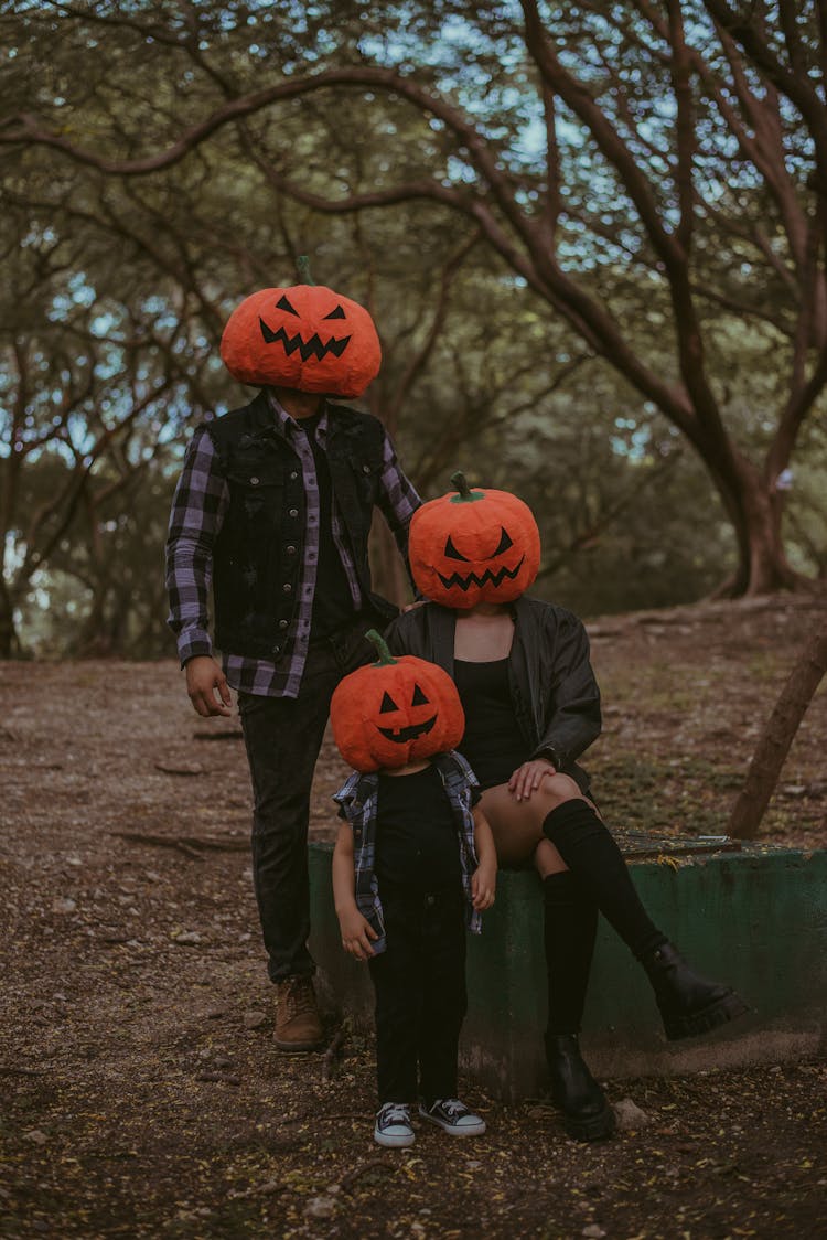 Family Standing On Forest Wearing Carved Pumpkins Over Their Head