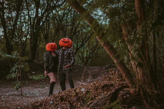 A couple wearing pumpkin masks in a spooky, wooded area, perfect for Halloween vibes.