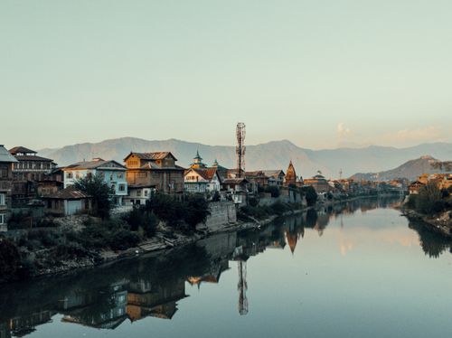 Free Beautiful riverside town with reflections on calm water and mountains in the background. Stock Photo