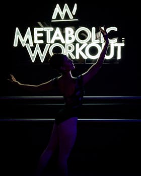 Silhouette of a ballerina dancing under a neon metabolic workout sign.