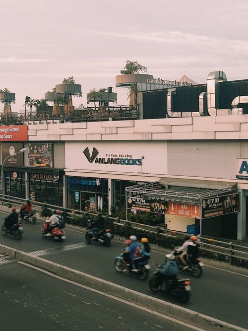 Free Busy urban street with motorcycles passing by a row of shops in the evening. Stock Photo