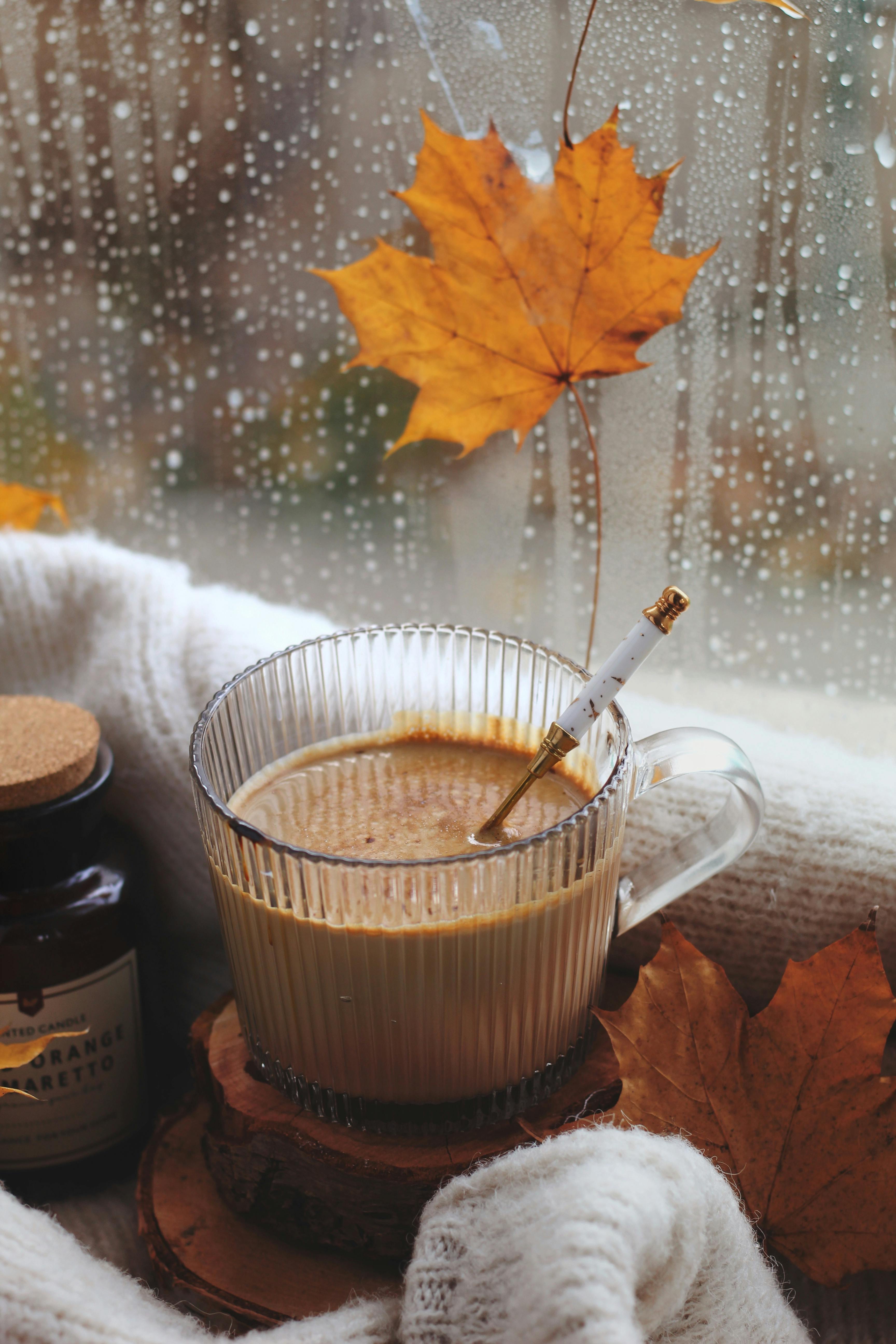 Warm cup of coffee with autumn leaves by a rainy windowsill, creating a cozy atmosphere.