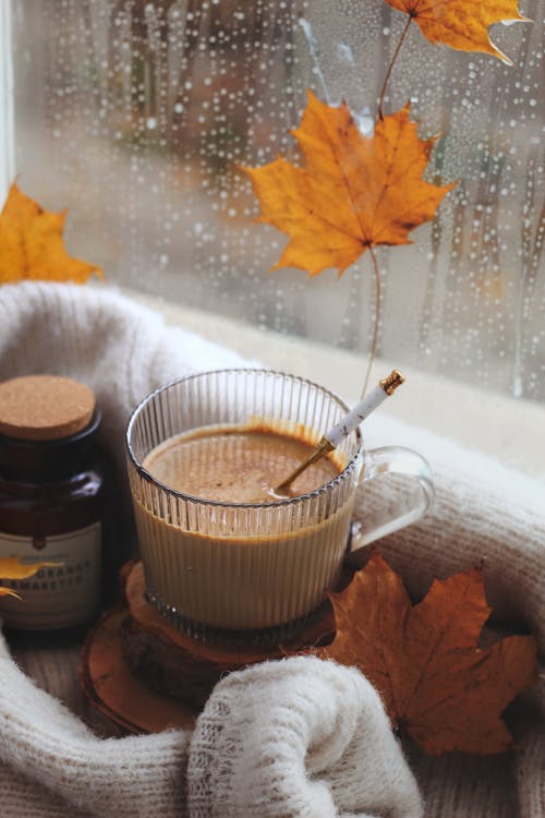 Cup of Coffee next to a Wet Window with Yellow Maple Leaves 