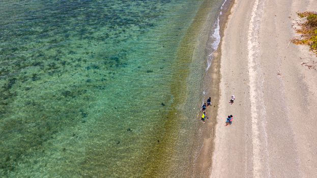 Aerial shot of a sandy beach with people by the turquoise sea, perfect for travel and leisure concepts.
