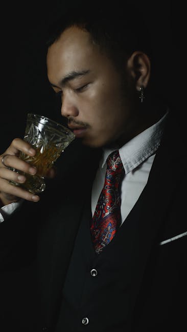 Close-up of a man sipping whiskey in a black suit and colorful tie, exuding elegance.
