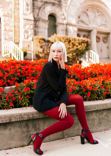 Stylish woman sitting in front of a vibrant flower bed in Des Moines, wearing bold red tights.