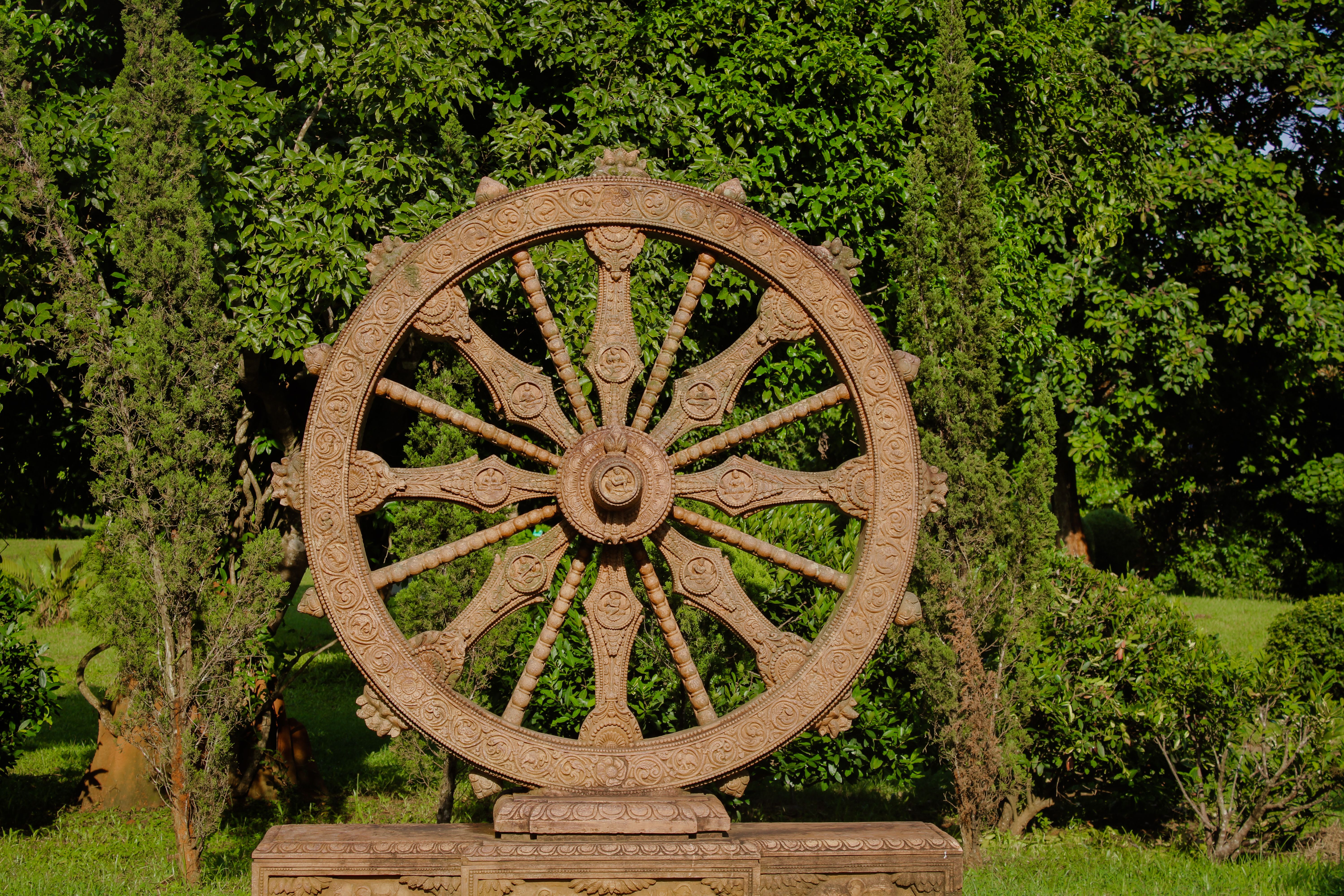 A detailed stone sculpture resembling a wheel set in a lush garden landscape, showcasing intricate artistry.