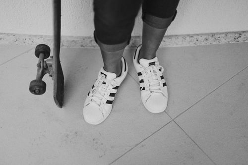 Free Black and white photo of legs in sneakers next to a skateboard indoors. Stock Photo
