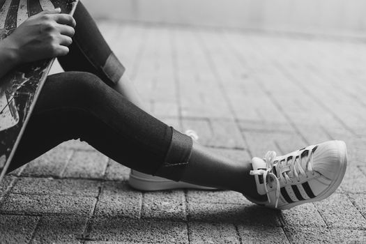 Close-up of a skater's legs in jeans and sneakers, holding a skateboard.