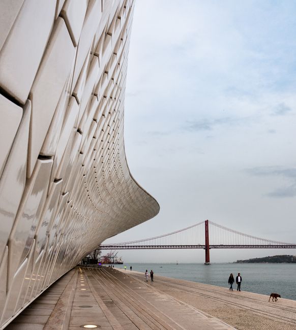 Sleek architectural facade with Lisbon's iconic bridge in the background.