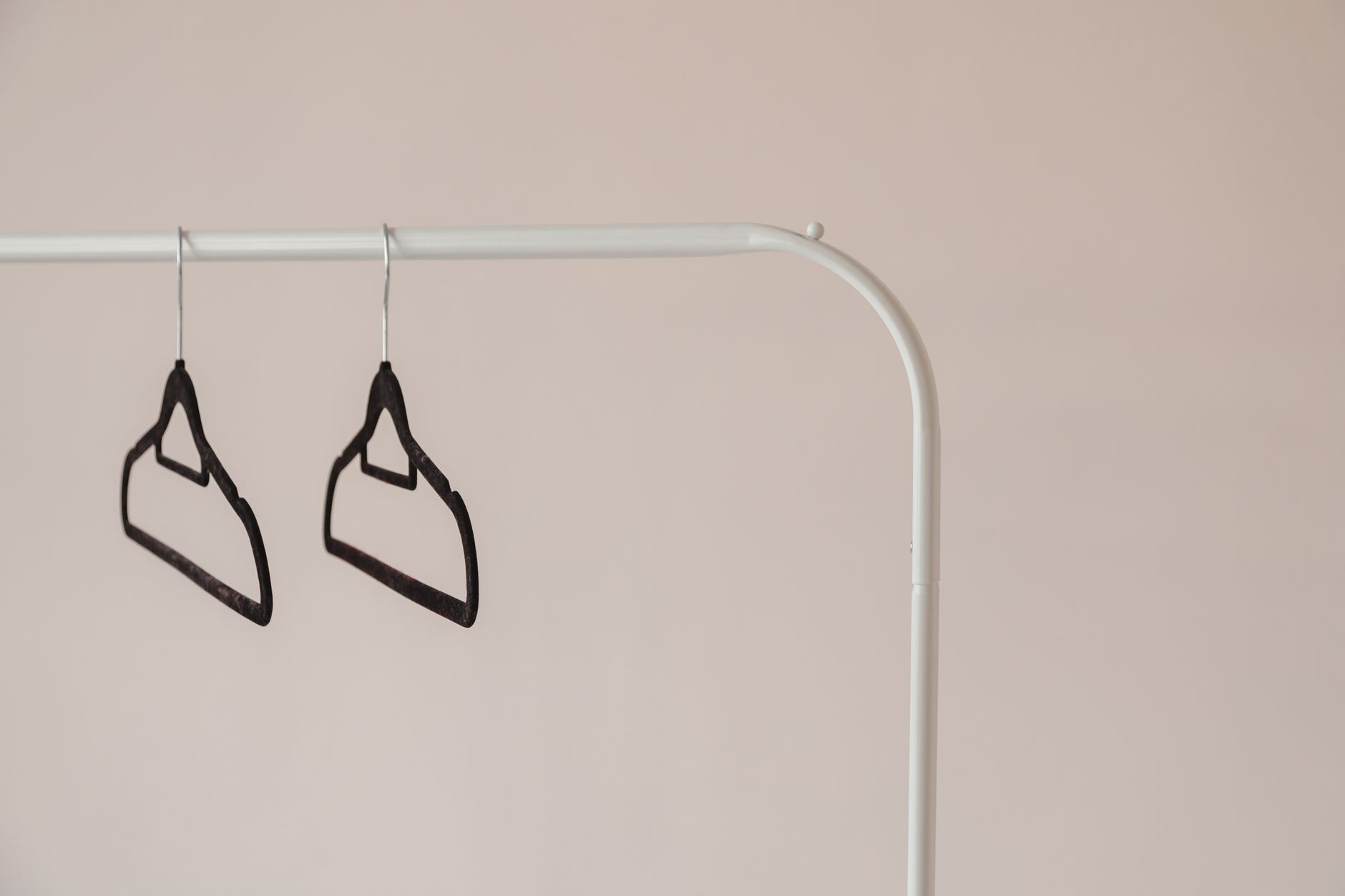 A simple, modern clothing rack with two black hangers against a neutral background.