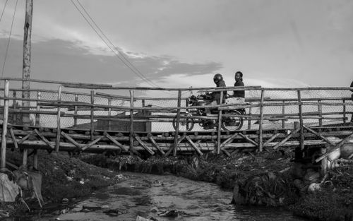 Free Two people ride a motorbike across a rustic wooden bridge in black and white style. Stock Photo