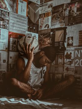 A pensive African man sitting indoors with a basketball in Awka, Nigeria.