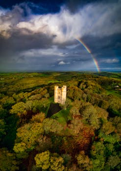 Aerial shot of Haldon Belvedere in autumn colors with a vivid rainbow overhead, Exeter, UK.