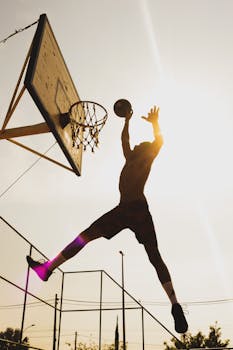 Basketball player jumping to dunk with silhouette against the bright sun.