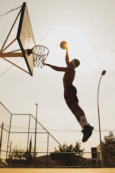 A silhouette of a basketball player dunking in an outdoor court during the daytime.