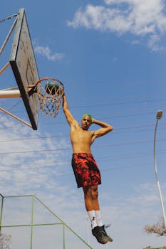 A dynamic shot of a young male athlete performing a slam dunk on an outdoor basketball court.