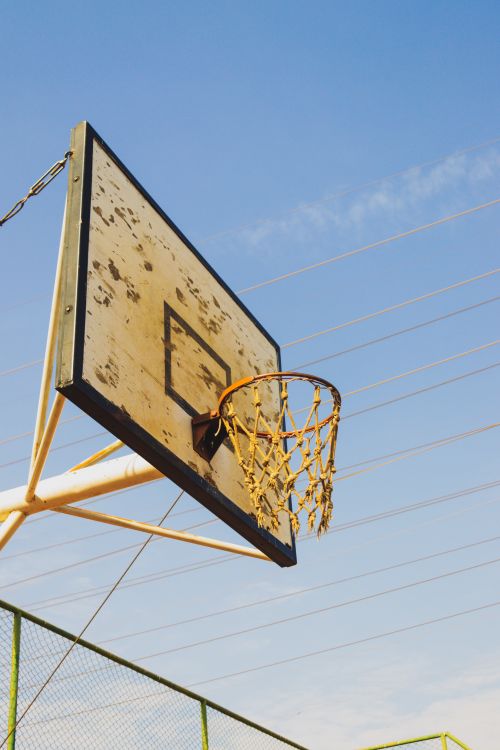 Free A weathered basketball hoop and backboard against a clear blue sky, symbolizing nostalgia. Stock Photo