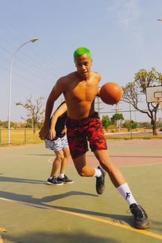 Male athlete with green hair playing basketball outdoors, showcasing dynamic movement and energy.