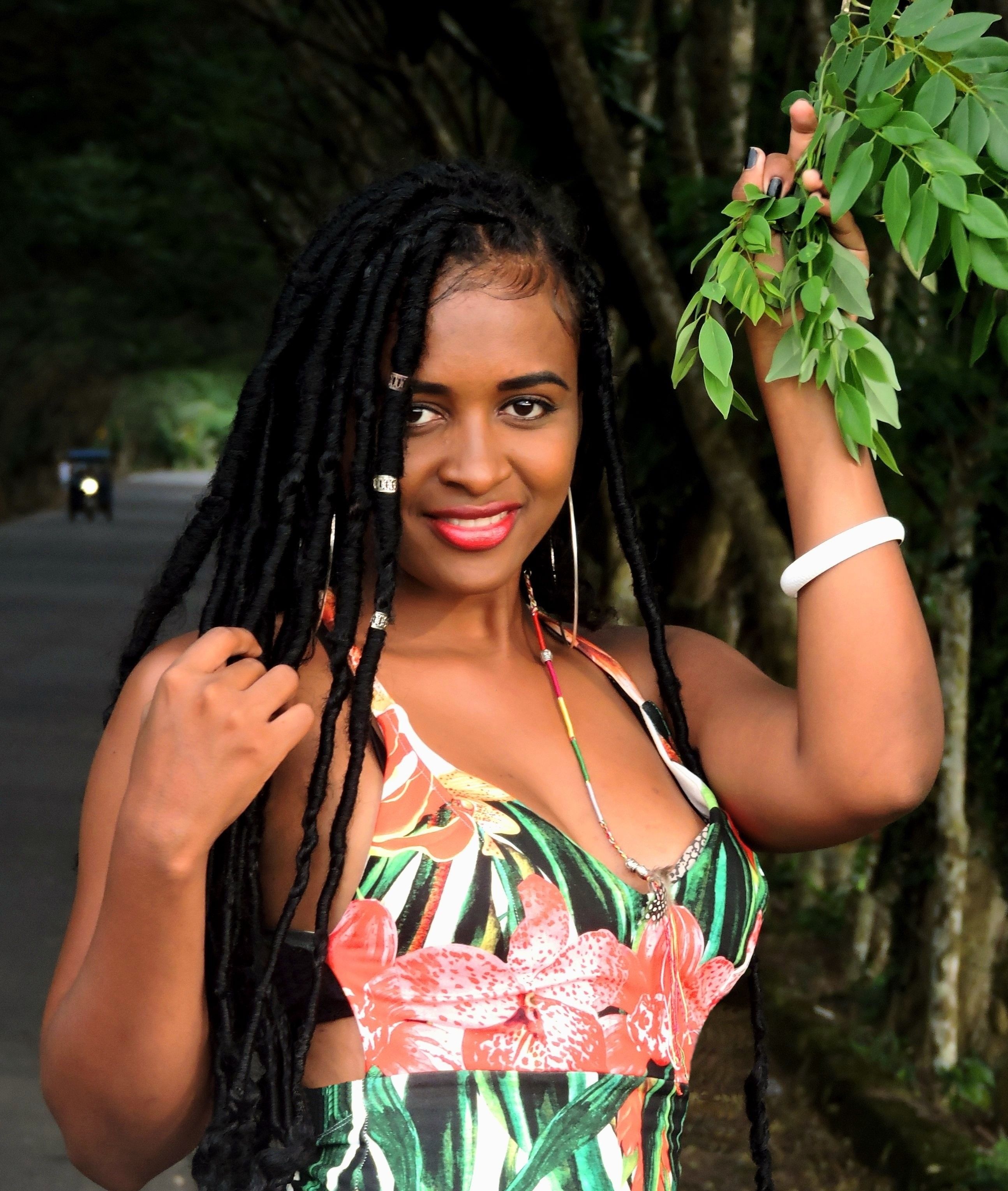 Confident woman with braided hair poses in a colorful dress amidst a lush green backdrop.