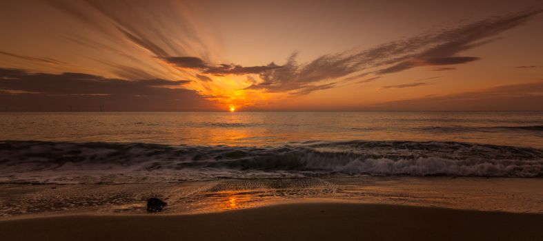 Dramatic sunset over the ocean with waves crashing onto the sandy shore.