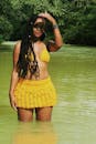 一位穿着黄色比基尼的黑人妇女在绿树环绕的河中自信地摆着姿势