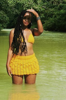 一位穿着黄色比基尼的黑人妇女在绿树环绕的河中自信地摆着姿势