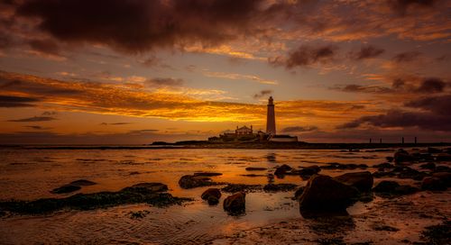 Free Stunning sunset view over a rocky shoreline with a prominent lighthouse on the horizon. Stock Photo