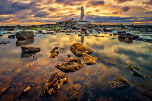 Free Captivating sunset view of St Mary's Lighthouse with reflective rocky shore in the UK. Stock Photo