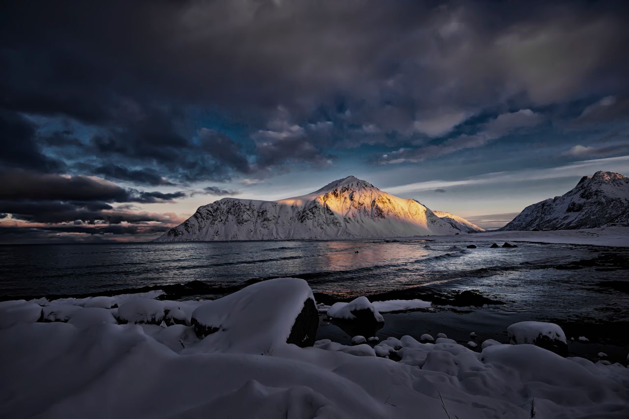 dramatic sunset over snow covered mountains by the cold arctic sea in