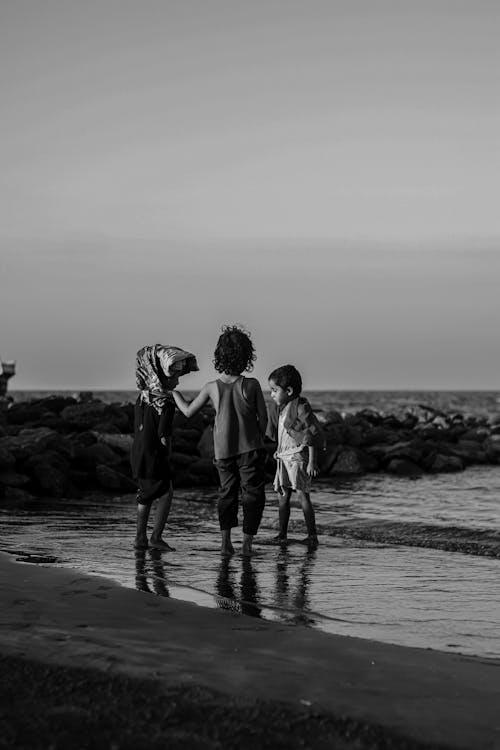 Grayscale Photo of Kids Standing on the Beach