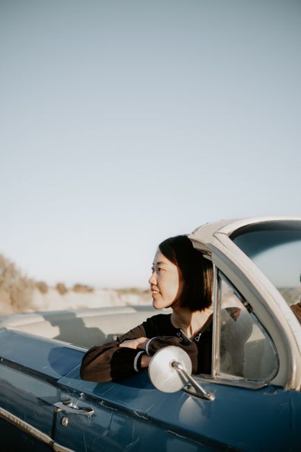 A woman relaxes in a classic convertible car on a sunny day, enjoying the road trip