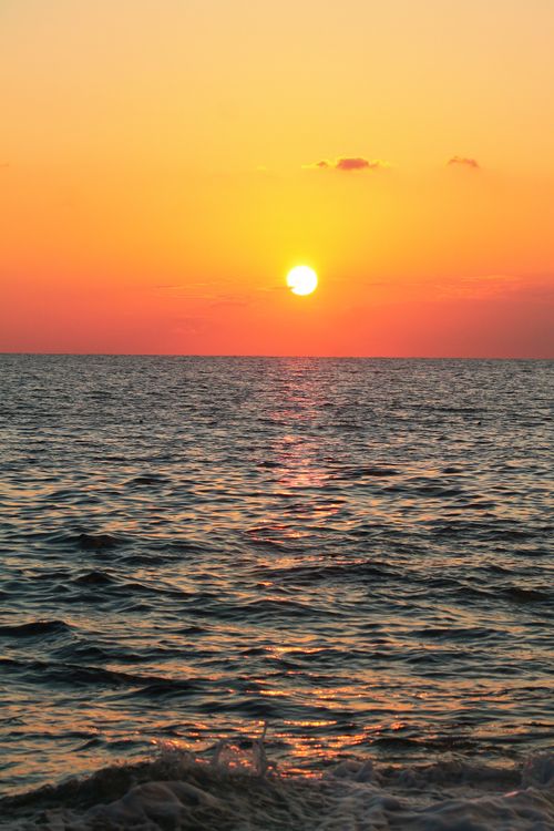 Free A breathtaking view of the sunset over the ocean, featuring vivid orange and yellow hues reflected on the sea. Stock Photo