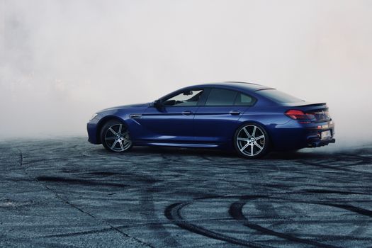 A sleek blue car performing a dramatic drift on an open asphalt area in Turkey.