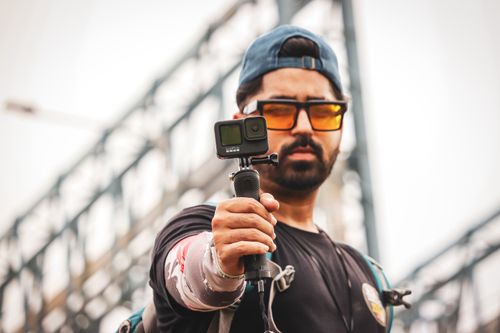 Free Asian man with GoPro filming outdoors, wearing sunglasses and a black shirt. Stock Photo