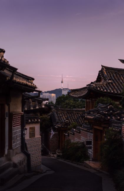 Charming Seoul street with traditional rooftops and Namsan Tower at sunset.