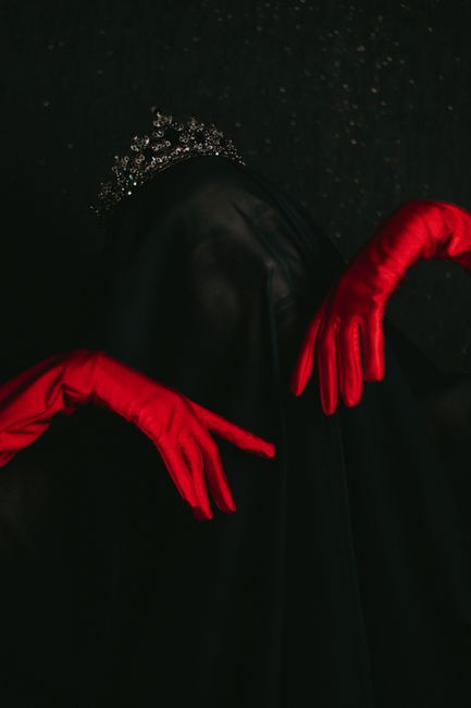 Ethereal portrait of a veiled woman in a crown with red gloves, creating a spooky atmosphere.