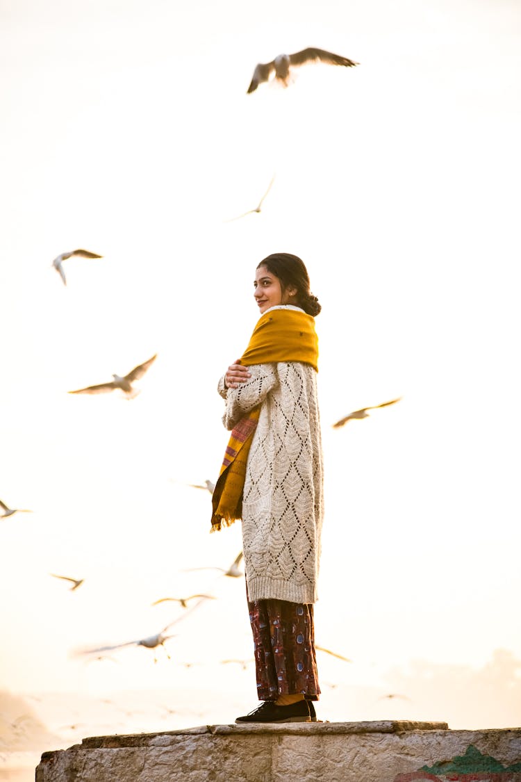 Woman Standing On Ledge Looking At Flying Birds